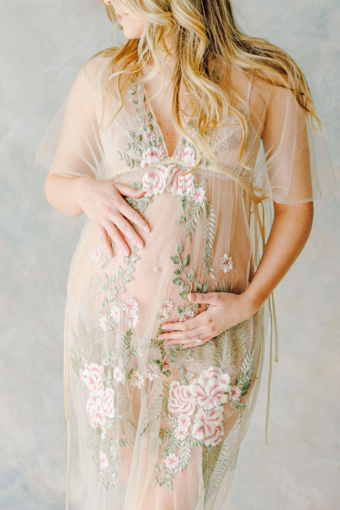 mom in a sheer dress holding her pregnant belly looking down